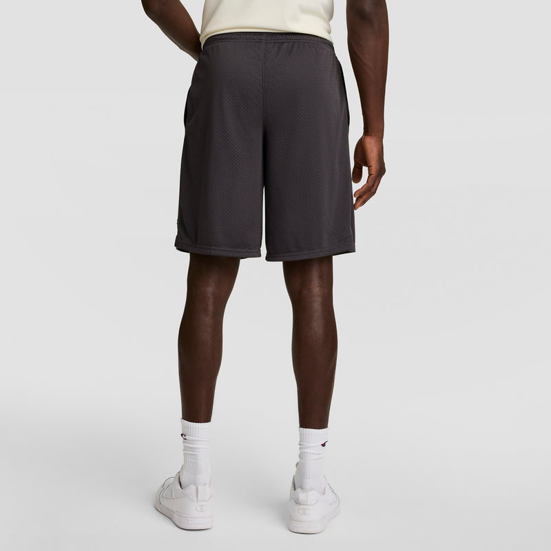 A person in a cream shirt, white crew socks, white sneakers, and Champion 9" Classic Mesh Shorts with a C Logo stands with their back to the camera against a plain light background.