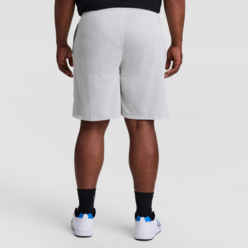 A person wearing Champion 9" Classic Mesh Shorts, C Logo - Big & Tall in white, paired with black socks and white sneakers, stands with their back to the camera against a plain light background.