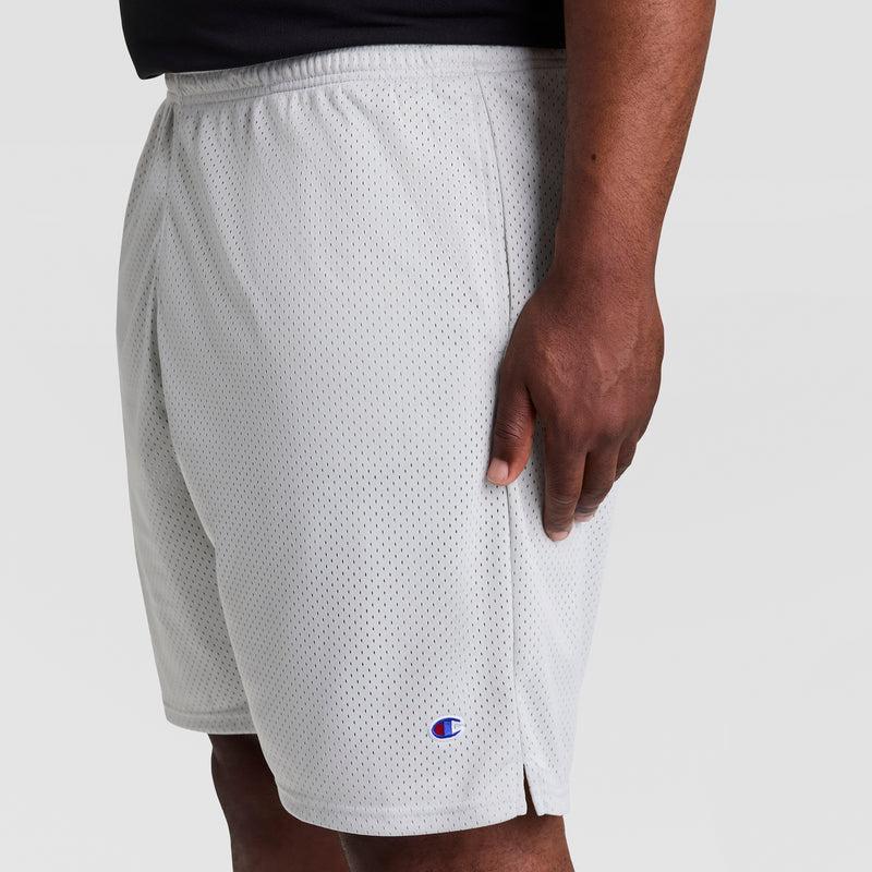 A person wears Champion 9" Classic Mesh Shorts, C Logo - Big & Tall in light gray, featuring the iconic logo near the hem. They stand against a plain light background with their arm resting by their side.