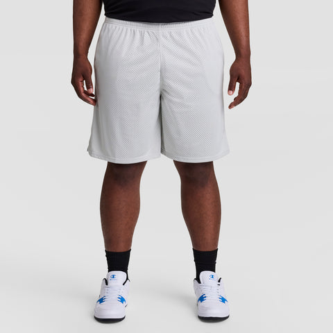 A person models the Champion 9" Classic Mesh Shorts, C Logo - Big & Tall in white, paired with black socks and white sneakers with blue accents, standing against a plain light gray background. The image is cropped waist down.