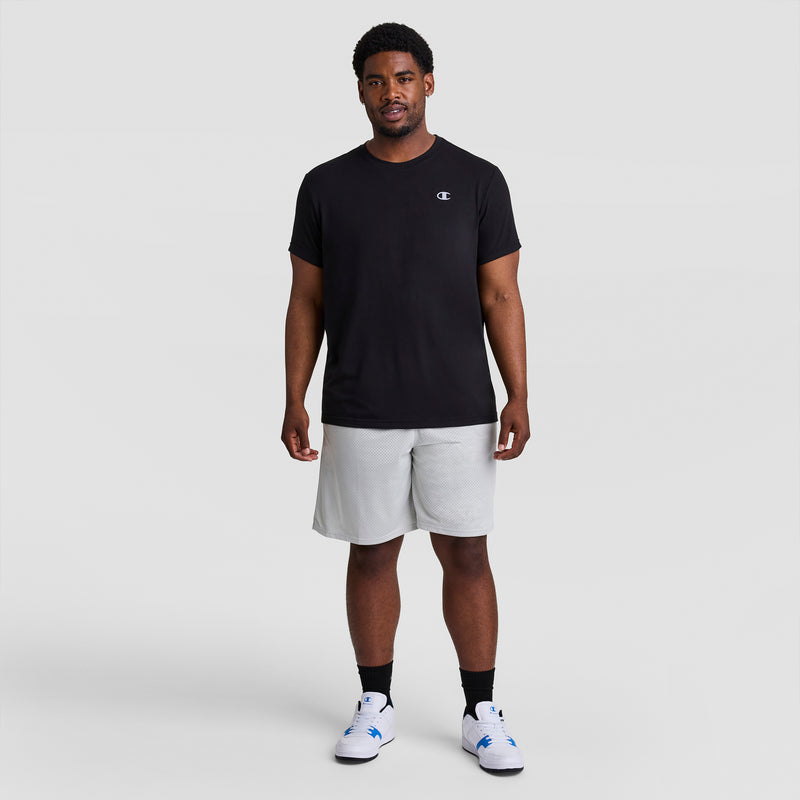 A man stands facing forward, wearing a black Champion t-shirt, Champion 9" Classic Mesh Shorts (C Logo - Big & Tall) in light gray, black socks, and white sneakers against a plain light gray background.
