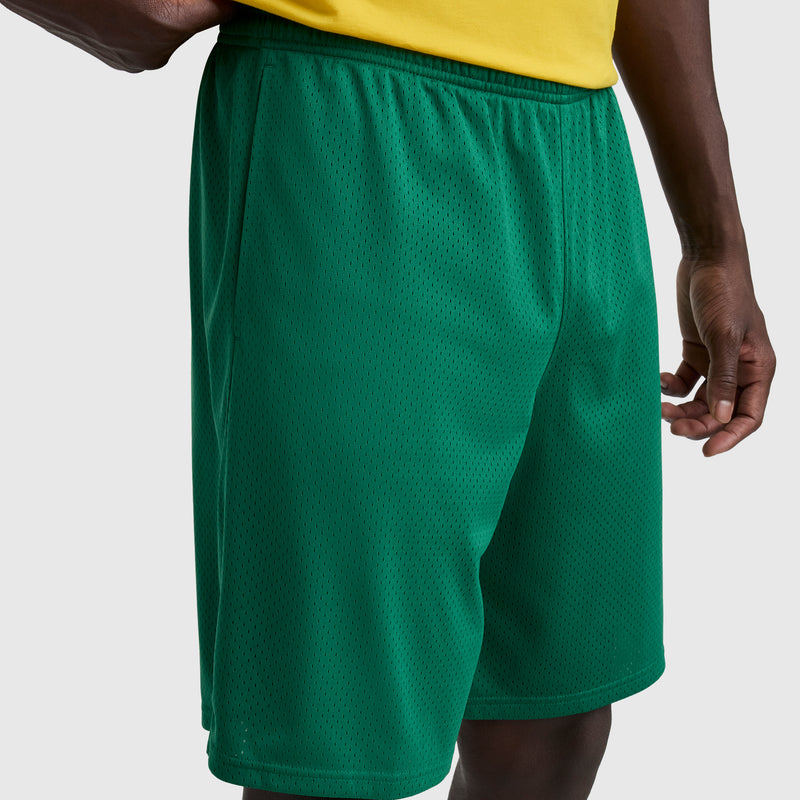A person is shown from the lower torso to upper legs, wearing a yellow shirt and Champion 9" Classic Mesh Shorts with C Logo in green, standing against a plain light gray background.