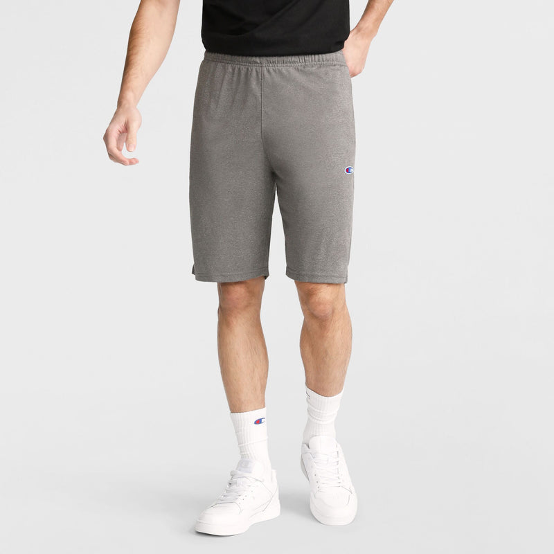 A person wearing a black shirt, white socks, white sneakers, and Champion 9" Lightweight Lounge Shorts with a C Patch Logo stands against a plain background.