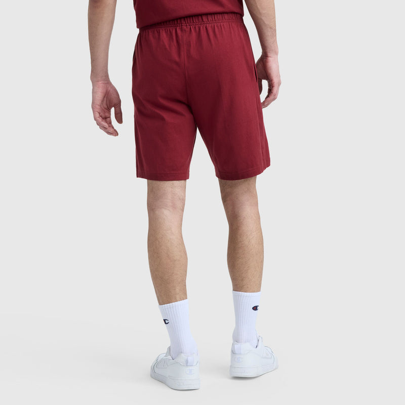 A person stands facing away, wearing Champion's 9" Lightweight Lounge Shorts with C Patch Logo, a matching maroon T-shirt, white crew socks with a blue and red logo, and white sneakers against a plain light background.