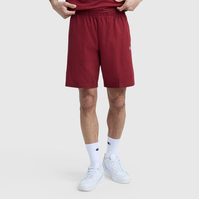 A person models Champion 9" Lightweight Lounge Shorts with C Patch Logo in maroon, paired with white socks and sneakers, standing against a plain light gray background. Only the lower half of the body is shown.