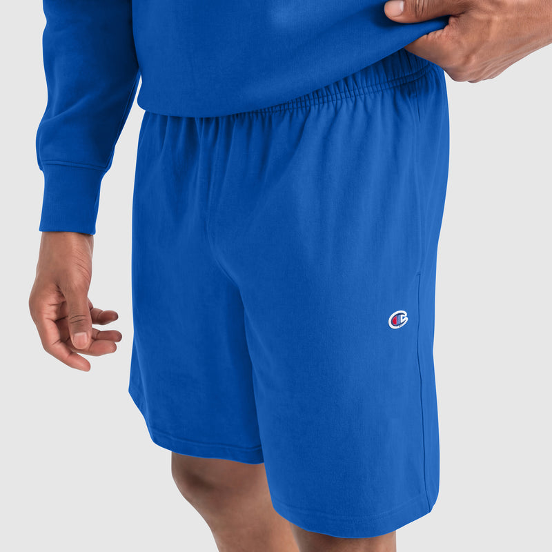 A person wears bright blue Champion 9" Lightweight Lounge Shorts with a C Patch Logo and a matching blue sweatshirt, one hand on their waist. The cotton jersey shorts are perfect for a casual lounge look.