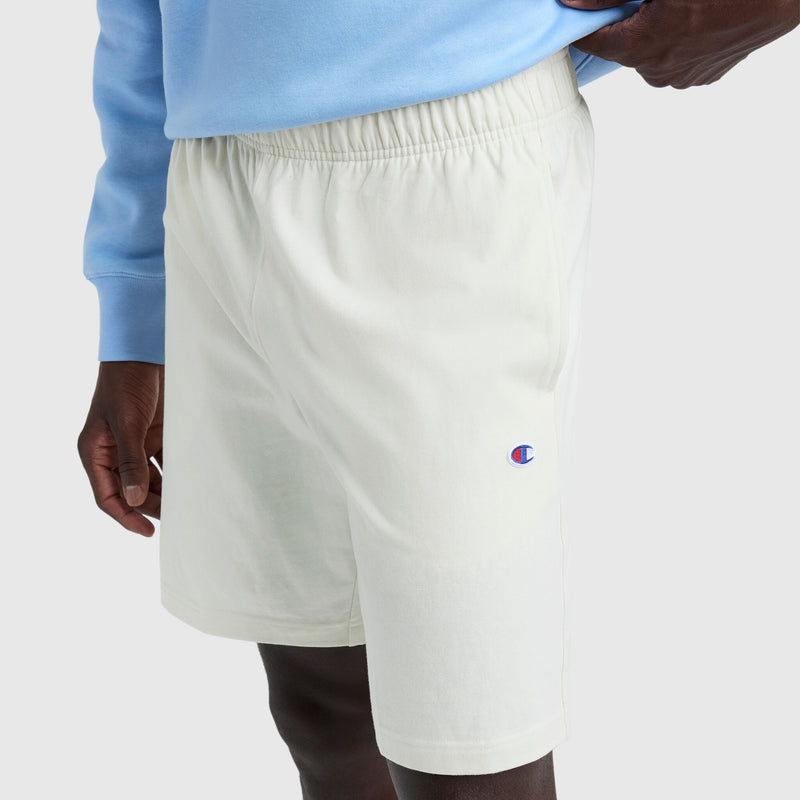 A person is standing against a plain background, showing only their lower torso and upper legs while wearing Champion 9" Lightweight Lounge Shorts with the C Patch Logo in off-white and an elastic waistband.