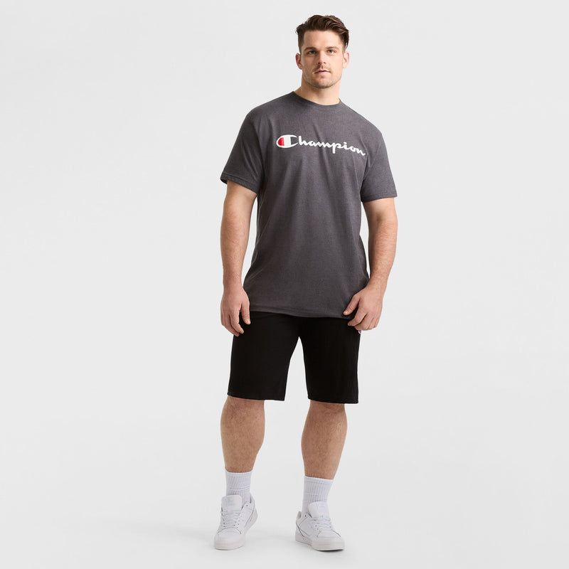 A man stands facing forward against a plain white background, wearing a dark gray Champion t-shirt, the Champion 9" Lightweight Lounge Shorts with C Patch Logo - Big & Tall in black, white socks, and white sneakers.