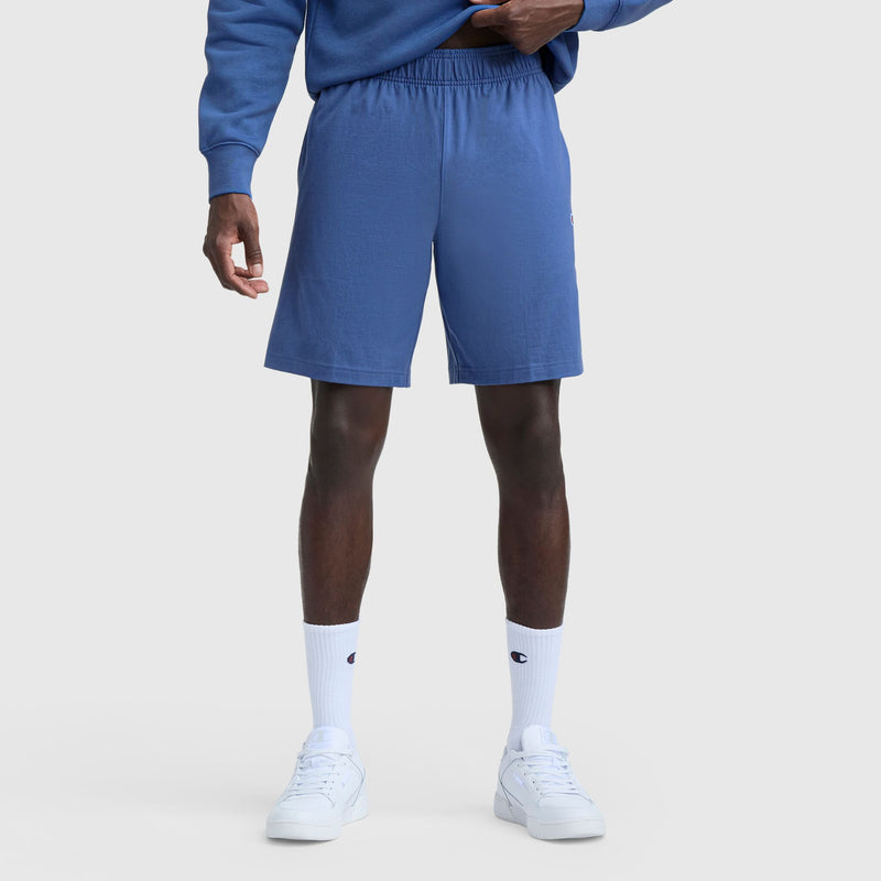 A person wears Champion 9" Lightweight Lounge Shorts with C Patch Logo, paired with white socks and sneakers, against a light background. Only the lower body is visible; the jersey fabric provides comfort and an adjustable fit offers style.