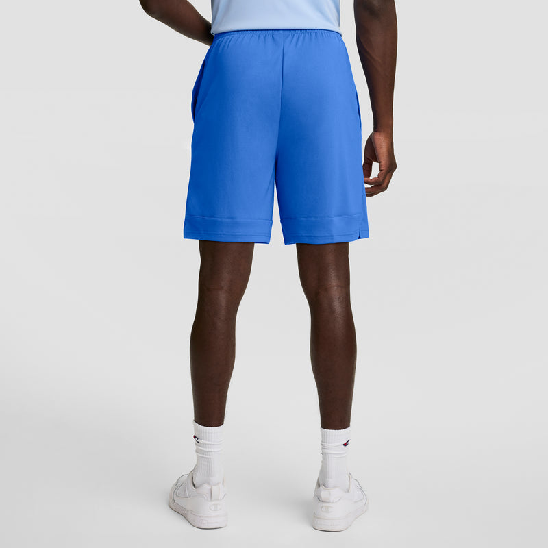 A person wearing a light blue shirt, Champion 7" Moisture Wicking Sport Shorts in bright blue, white socks, and white sneakers stands with their back to the camera against a plain white background.