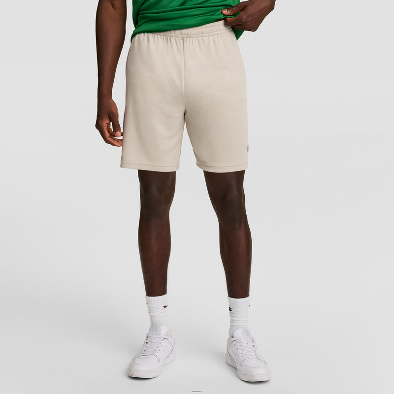 A person in a green shirt, Champion 7" Moisture Wicking Sport Shorts, white crew socks, and white sneakers stands against a plain light background. Their face is not visible.