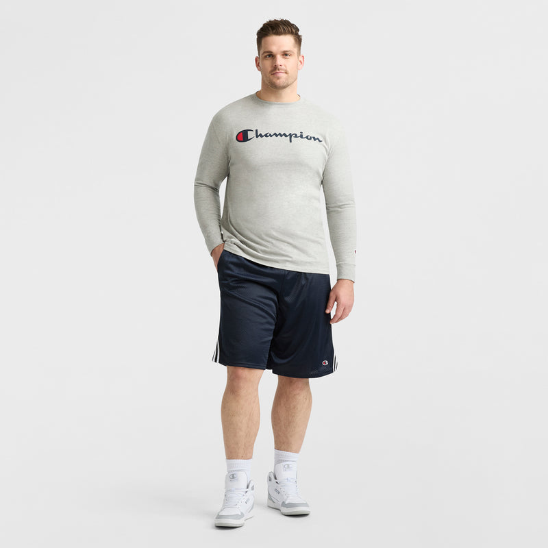 A man stands against a white background wearing a light gray long-sleeve shirt, Champion 10" Lacrosse Mesh Shorts - Big & Tall in navy, white crew socks, and white sneakers.