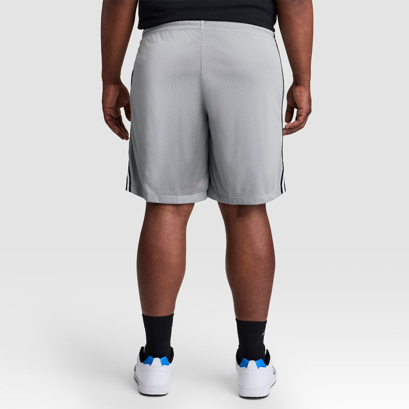 A person stands facing away, wearing Champion 10" Lacrosse Mesh Shorts - Big & Tall in light gray with a black shirt, black socks, and white sneakers with blue accents against a plain light background.