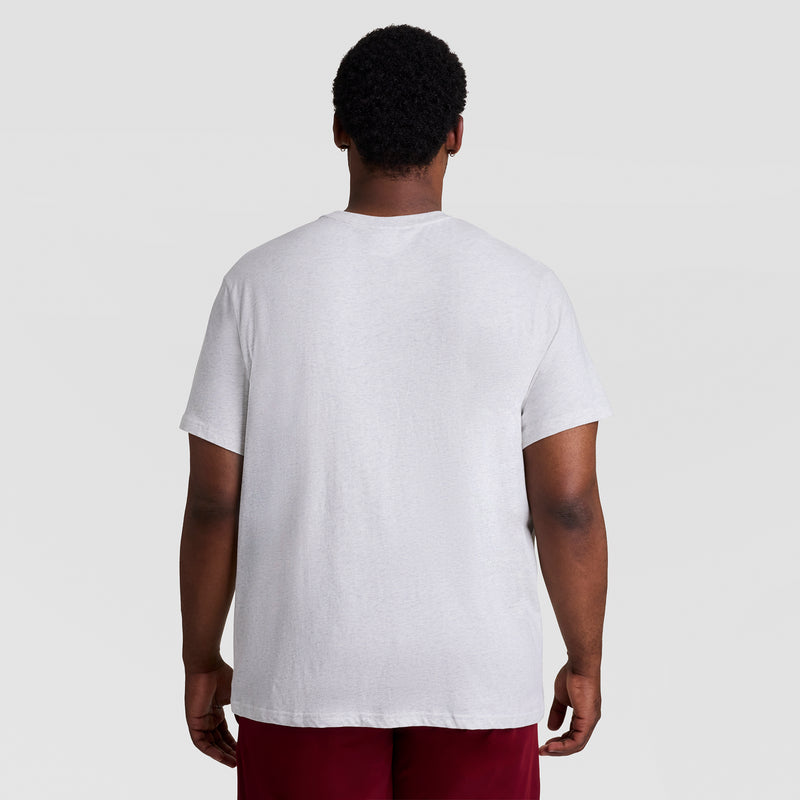 A man stands with his back to the camera, wearing a Champion Classic Graphic T-Shirt with a tonal script logo (Big & Tall) and red shorts against a light gray background.