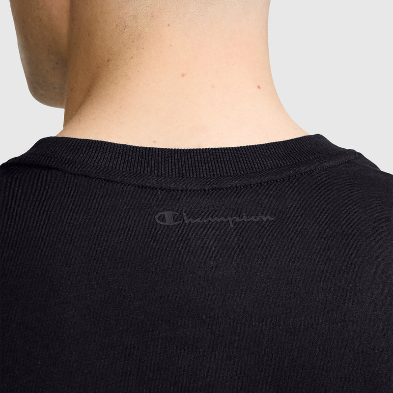 The back view of a person’s neck and upper shoulders wearing the Champion Classic Graphic T-Shirt, Tonal Script Logo, a black men’s tee featuring a subtle tonal script logo just below the collar. Made from 100% cotton, this T-shirt from Champion delivers comfort and style.