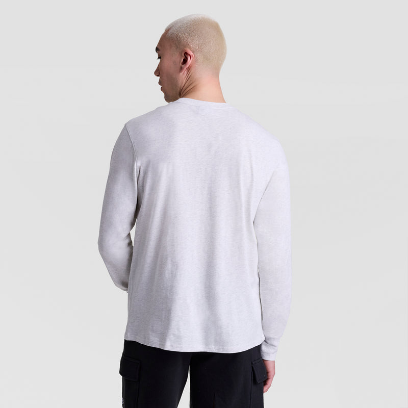 A person with short, light-colored hair stands with their back to the camera, wearing the Champion Classic Graphic Long-Sleeve T-Shirt, Script Logo and black pants against a plain light gray background.