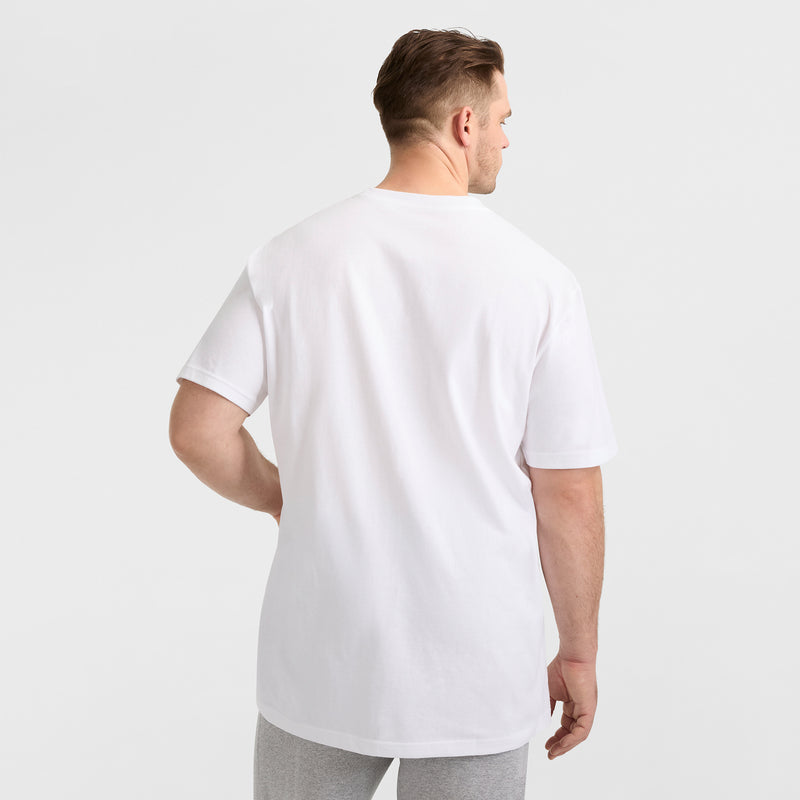 A man stands with his back to the camera in a classic Champion Script Logo Graphic T-Shirt (Big & Tall) and light gray pants against a white background—an understated look ideal for effortless streetwear style.