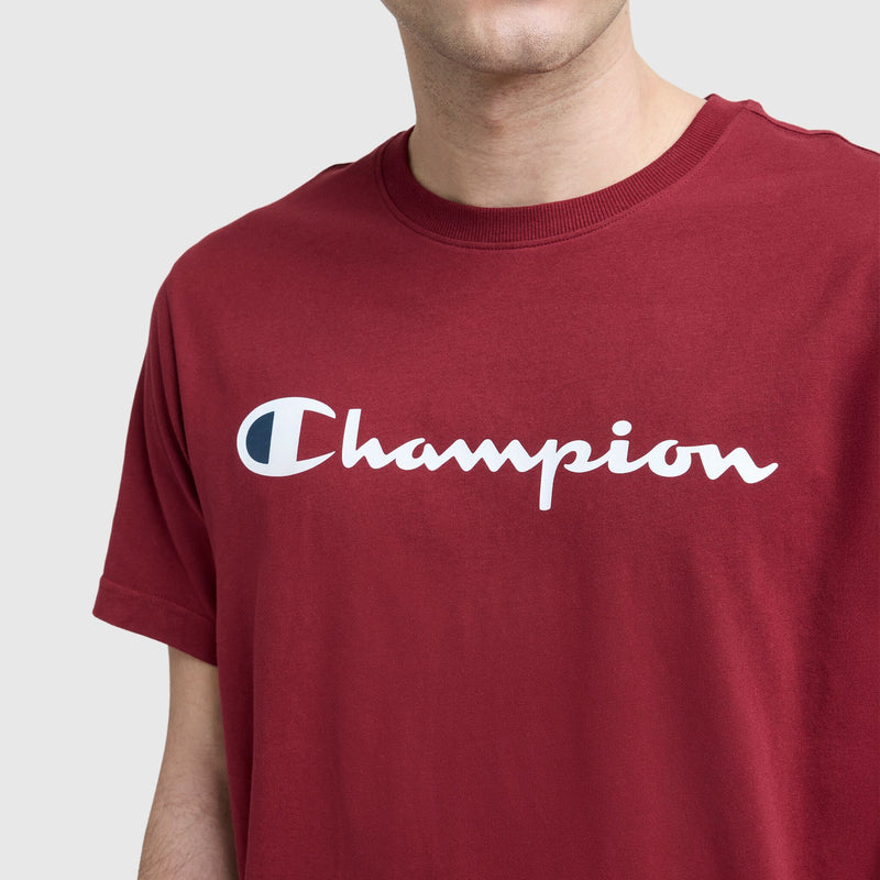 Wearing a maroon Champion Classic Graphic T-Shirt with the script logo in white on the front, only the lower face and upper body are visible against a plain background.