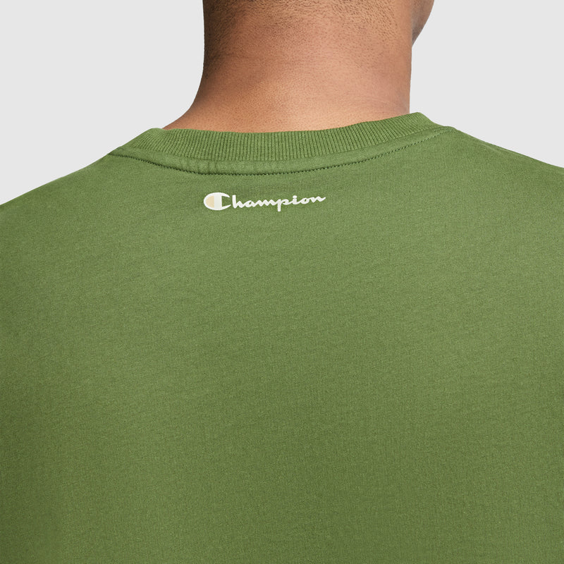 Close-up of the back of a green Champion Classic Graphic T-Shirt, Script Logo—a timeless streetwear staple—with the white Champion script logo printed near the neckline. The shirt is worn by a person, but only their neck and shoulders are visible from behind.
