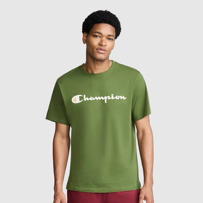 A man wearing a green Champion crewneck t-shirt with the brand's logo printed in white across the chest, set against a solid light gray background.
