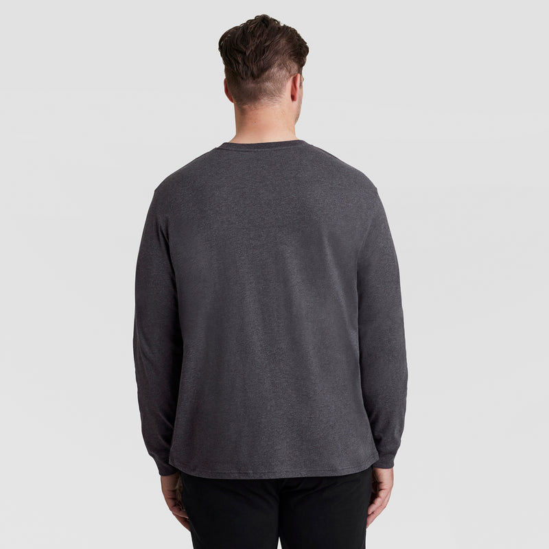 A man with short brown hair, facing away from the camera, wears a Champion Classic Long Sleeve T-Shirt with Embroidered C Logo (Big & Tall) and black pants against a plain light gray background.