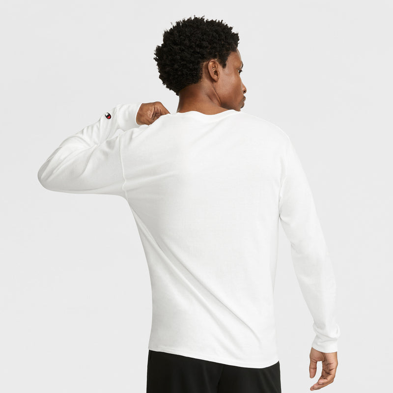 A person with short curly hair is seen from behind wearing the Champion Classic Long Sleeve T-Shirt with Embroidered C Logo and black pants, slightly lifting the shirt’s collar with their right hand against a plain white background.