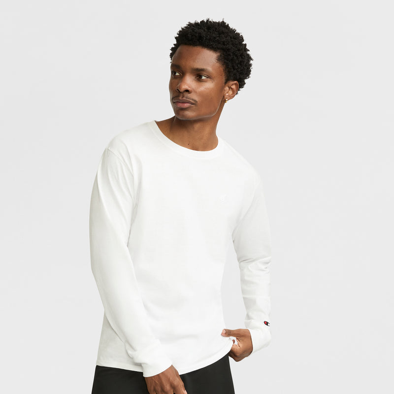 A man stands against a light gray background, wearing the Champion Classic Long Sleeve T-Shirt with Embroidered C Logo and black pants, looking to his left with his hand on his hip.
