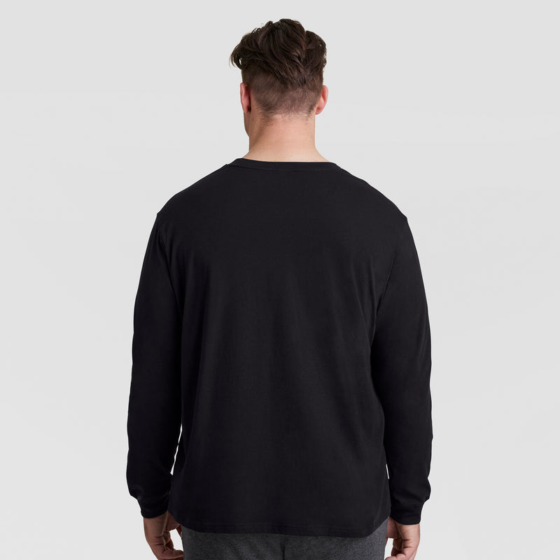 A man with short brown hair, seen from behind, wears a Champion Classic Long Sleeve T-Shirt with an embroidered C logo—Big & Tall—in black, paired with dark pants against a plain light gray background.