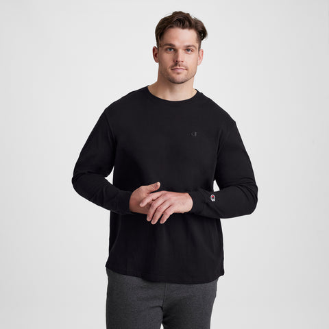 A man with short brown hair wears a black Champion Classic Long Sleeve T-Shirt, Embroidered C Logo - Big & Tall, and dark gray pants, standing against a plain light gray background and looking at the camera with a neutral expression.