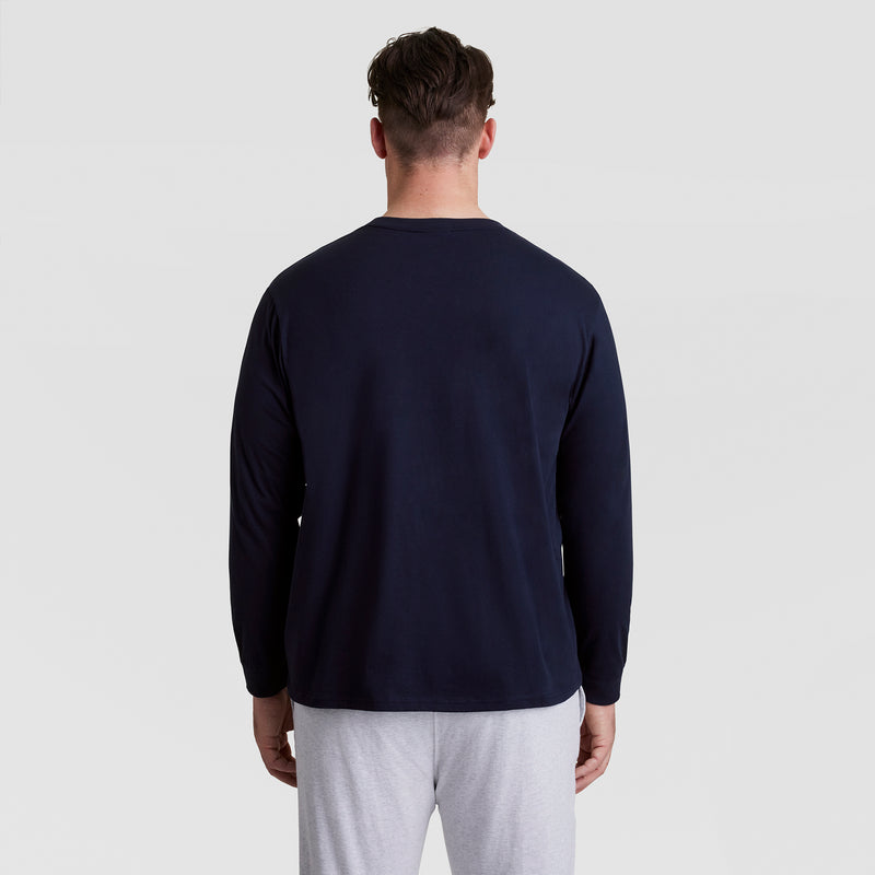 A person with short brown hair faces away from the camera, wearing a Champion Classic Long Sleeve T-Shirt, Embroidered C Logo - Big & Tall and light gray pants against a plain light background.