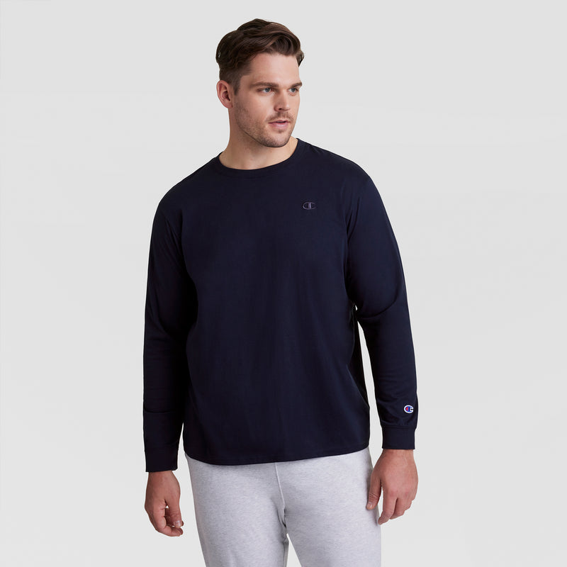 A man wearing a navy blue Champion Classic Long Sleeve T-Shirt with Embroidered C Logo (Big & Tall) stands against a plain light gray background, looking slightly to his left.
