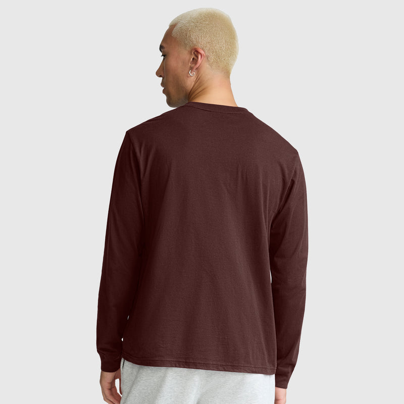 A person with short blond hair, seen from behind and standing against a plain light gray background, is wearing a Champion Classic Long Sleeve T-Shirt with an embroidered C logo in maroon and light gray pants.