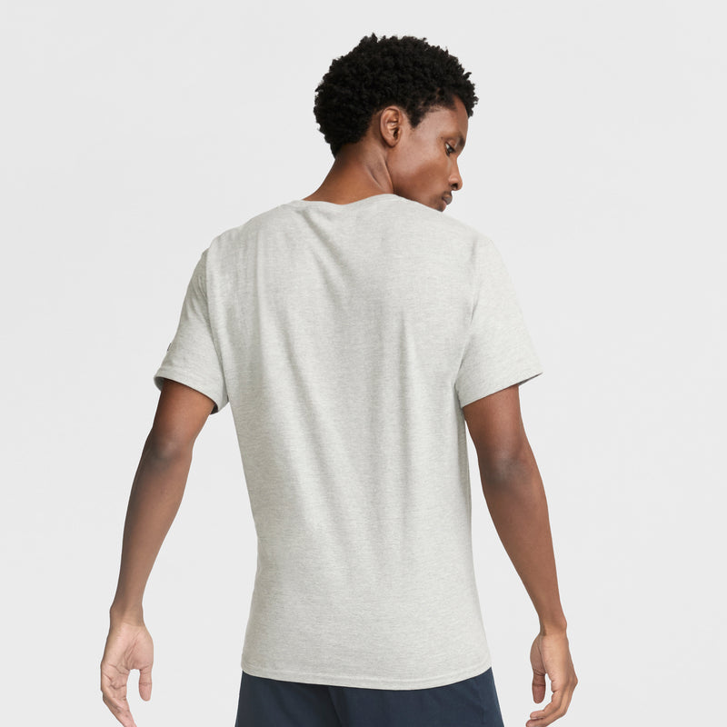 A person with short curly hair, wearing the Champion Classic T-Shirt, C Logo in light gray and dark shorts, stands facing away from the camera against a plain white background.