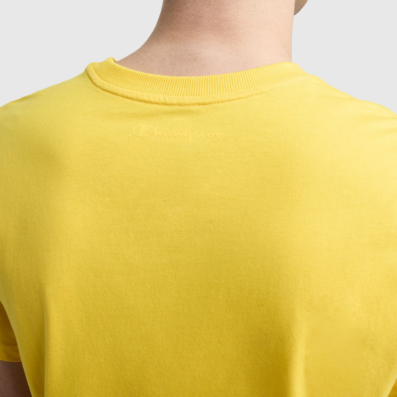 Close-up of a person wearing the Champion Classic T-Shirt, C Logo in bright yellow. The word "Champion" is subtly embroidered in matching yellow thread below the collar, adding a touch of classic style.