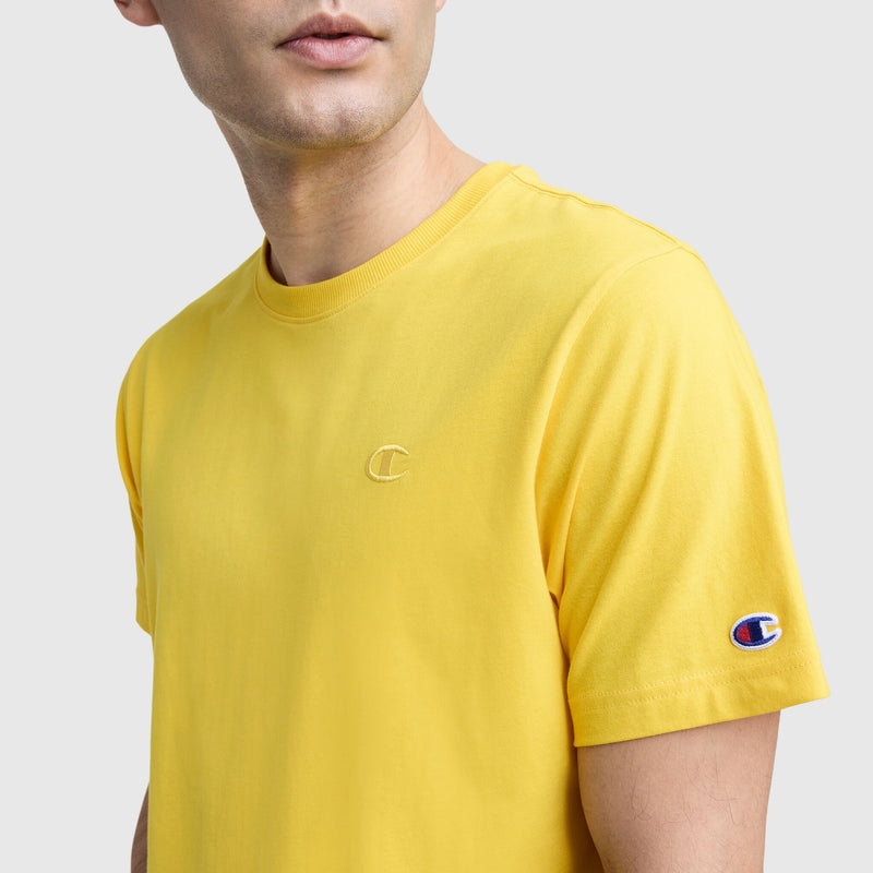 A man models the Champion Classic T-Shirt, C Logo—a bright yellow cotton tee with a sleeve logo and small chest “C”—against a plain light gray background.