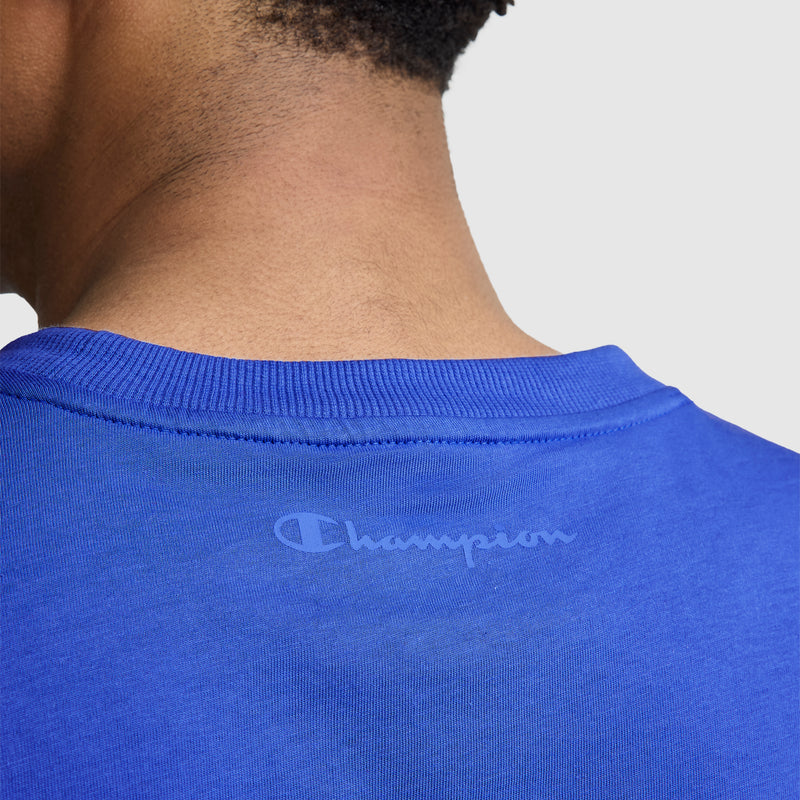 Close-up of the back of a person’s neck and shoulders wearing Champion's Classic T-Shirt, C Logo—a blue men’s tee crafted from soft cotton—featuring the Champion logo and wordmark in light blue on the upper back for timeless style.