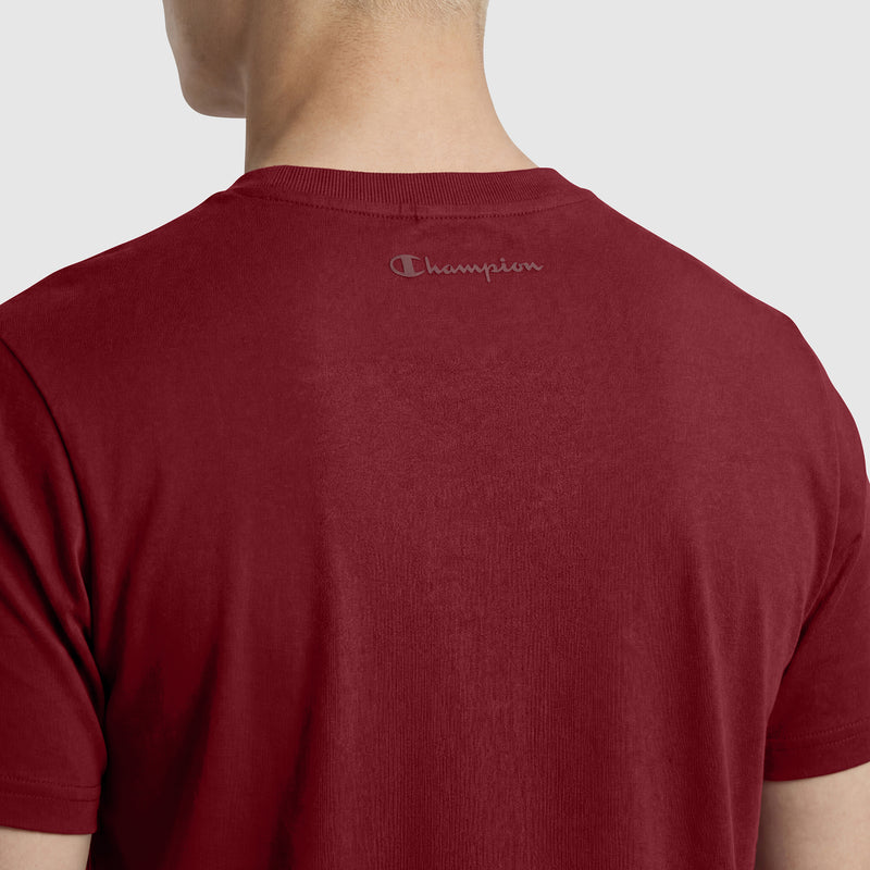 A person is seen from behind wearing the Champion Classic T-Shirt, C Logo in dark red, with "Champion" printed in small gray letters near the back neckline.