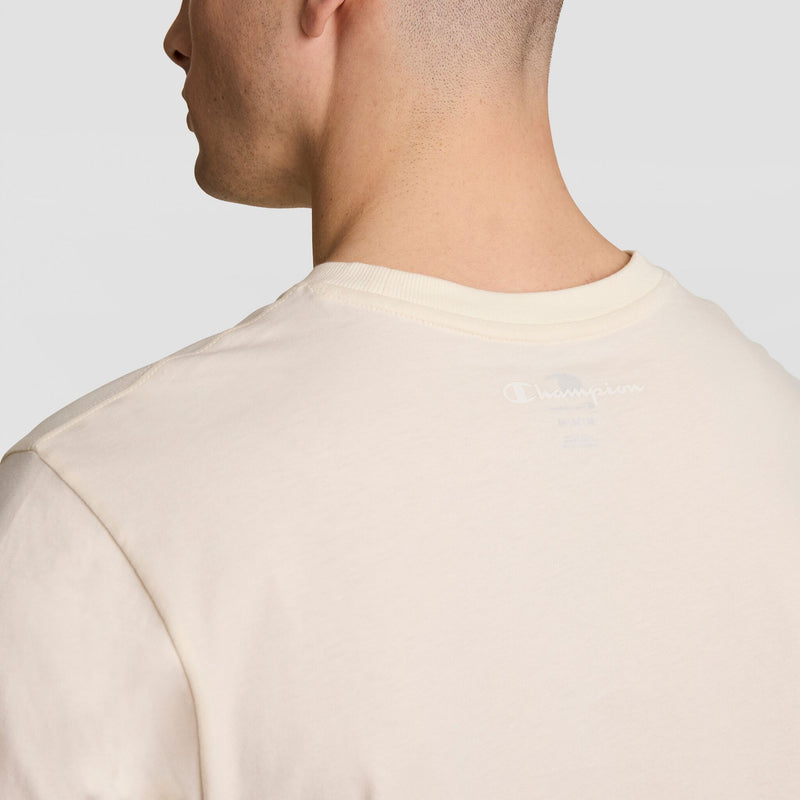 A close-up shows the back and side of a person wearing Champion's Classic T-Shirt, C Logo in cream, featuring the logo near the collar against a plain light background.