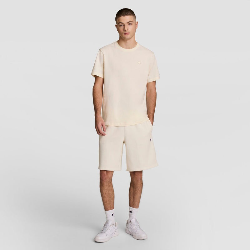 A young man stands facing forward in a Champion Classic T-Shirt, C Logo, paired with matching shorts, white socks, and sneakers against a plain light gray background.