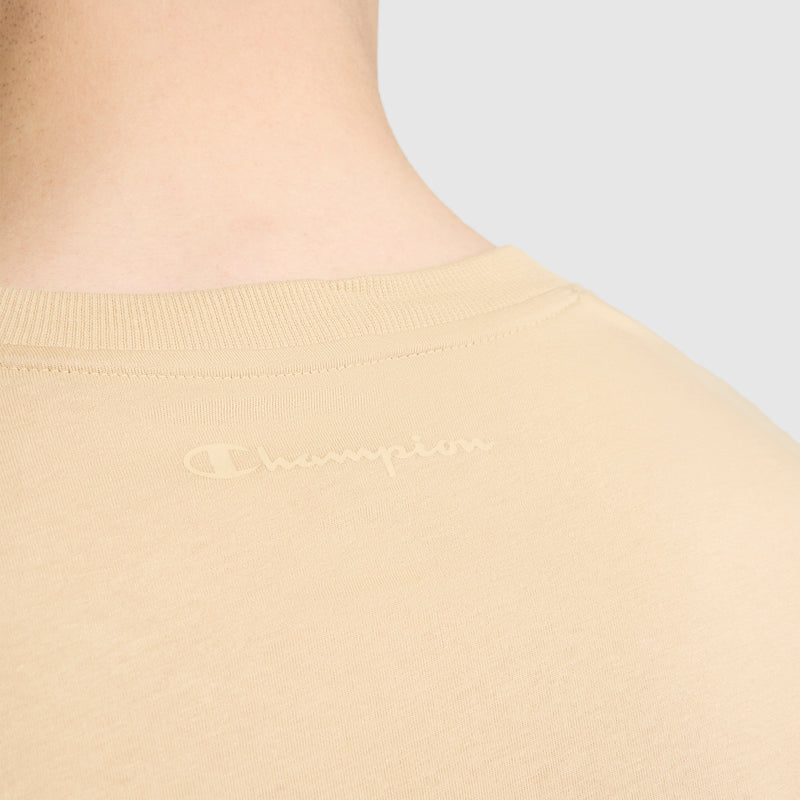 Close-up of the back of a person's neck and shoulders wearing the Classic T-Shirt, C Logo by Champion in beige, featuring a subtle Champion "C" logo printed near the neckline.