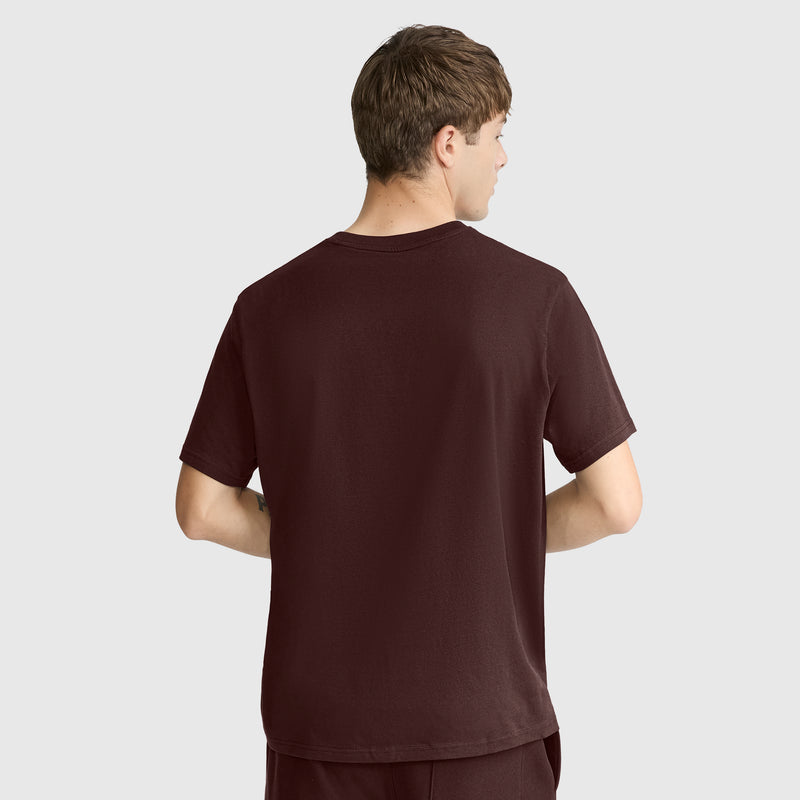 A person with short brown hair is standing with their back to the camera, wearing a Champion Classic T-Shirt, C Logo in plain dark brown and matching pants against a light gray background.
