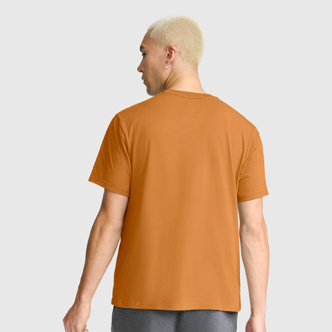 A person with short blond hair, wearing a Champion Classic T-Shirt, C Logo in orange and gray pants, is standing with their back to the camera against a plain light gray background.