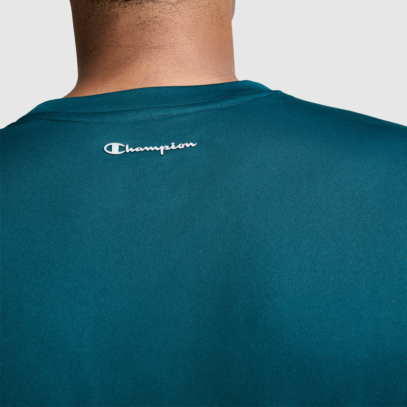 A close-up of a person wearing a teal Champion Sport T-Shirt, Reflective C Logo, with the white Champion logo displayed on the upper back. The image highlights the back of this men’s athletic shirt and the wearer’s neck.