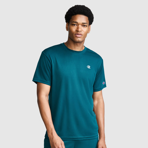 A man wearing a teal Champion Sport T-Shirt with a reflective C logo stands against a plain light gray background, looking at the camera with a neutral expression.