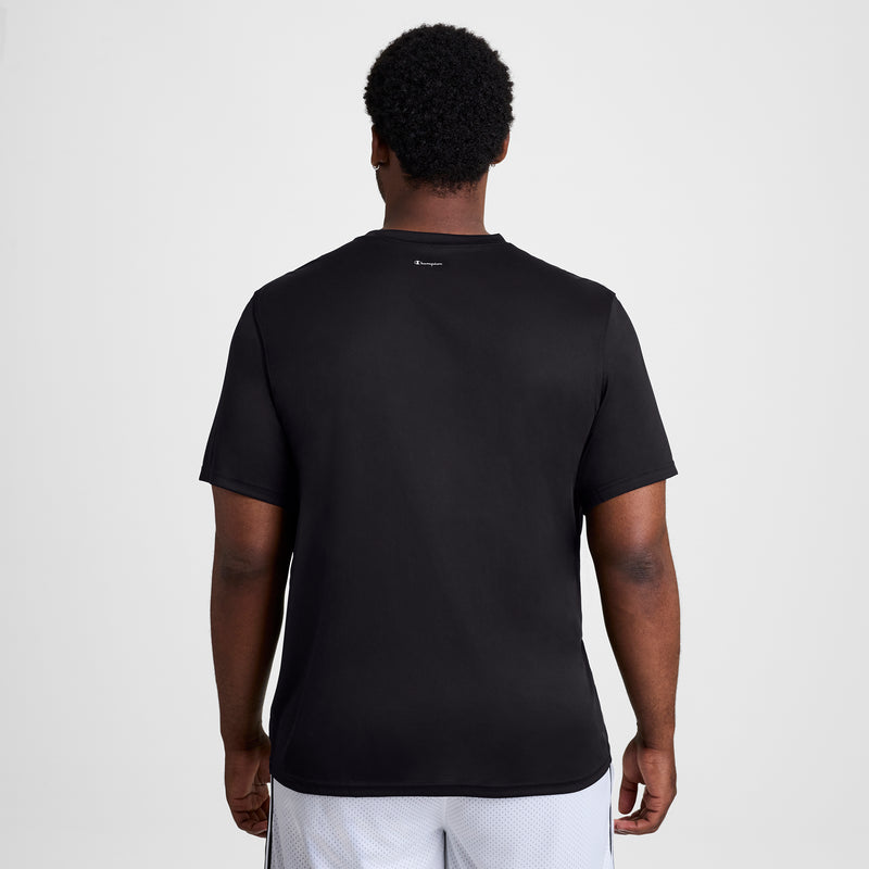 A man stands with his back to the camera wearing a Champion Sport T-Shirt, Reflective C Logo - Big & Tall, and white shorts against a plain white background.