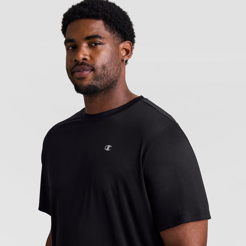 A man with short curly hair, facial hair, and an earring stands against a light gray background wearing a black Champion Sport T-Shirt, Reflective C Logo - Big & Tall, featuring a small reflective logo on the chest.