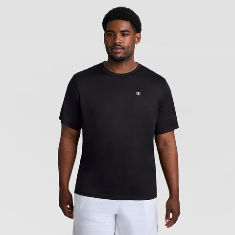 A man stands against a plain light gray background, wearing Champion's Sport T-Shirt, Reflective C Logo - Big & Tall in black and white athletic shorts. He faces forward with a neutral expression.