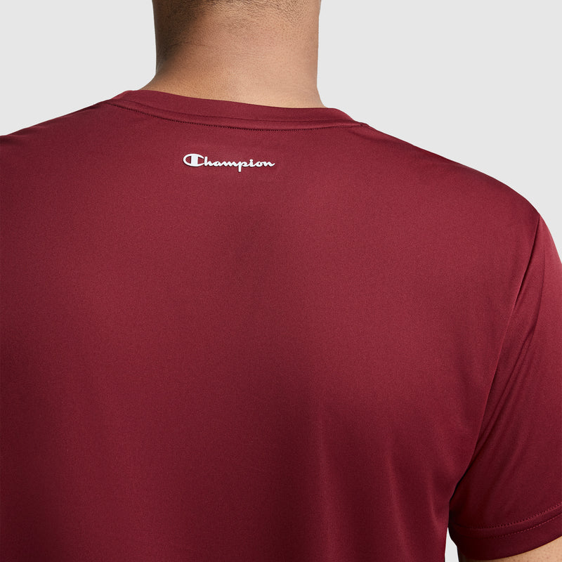 A person is shown from the back wearing a maroon Champion Sport T-Shirt, Reflective C Logo. The shirt features a reflective white Champion logo below the neckline and moisture-wicking technology. The background is plain and light gray.