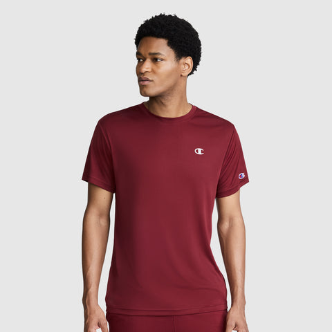 A man wearing a maroon Champion Sport T-Shirt, Reflective C Logo, with short sleeves stands against a plain light gray background, looking to his left. This Champion men’s athletic shirt features moisture-wicking technology for added comfort during any activity.