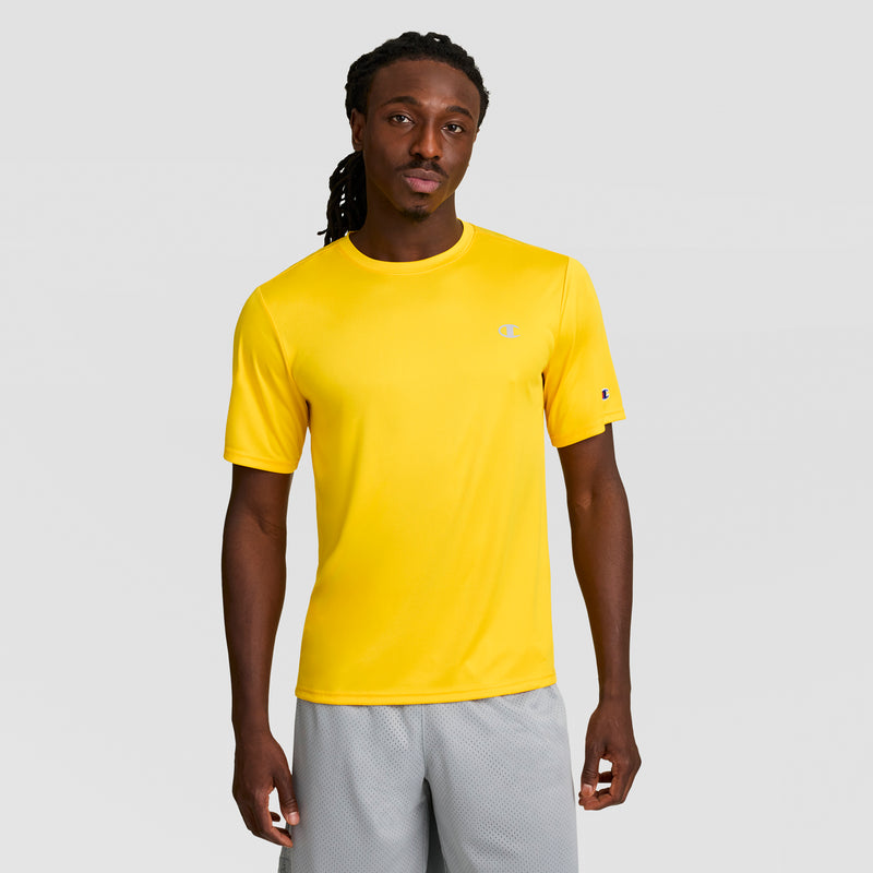 A man with long dreadlocks faces forward, wearing a Champion Sport T-Shirt with a reflective C logo and Double Dry tech in bright yellow, plus light gray shorts, all set against a plain light gray background.